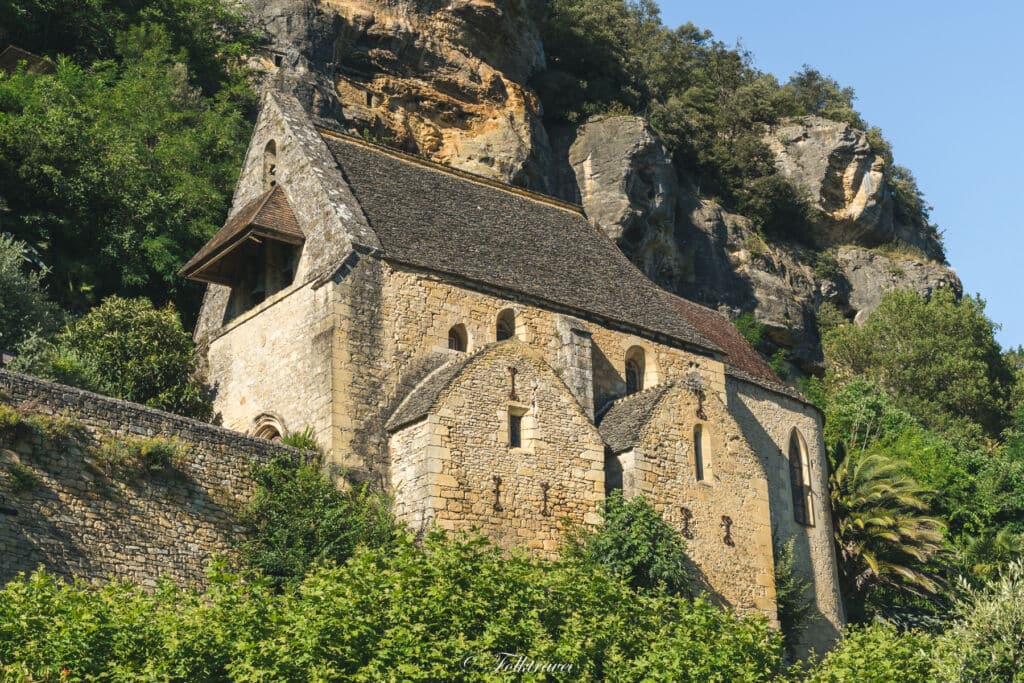  historic stone church nestled against a cliff, surrounded by lush greenery.
