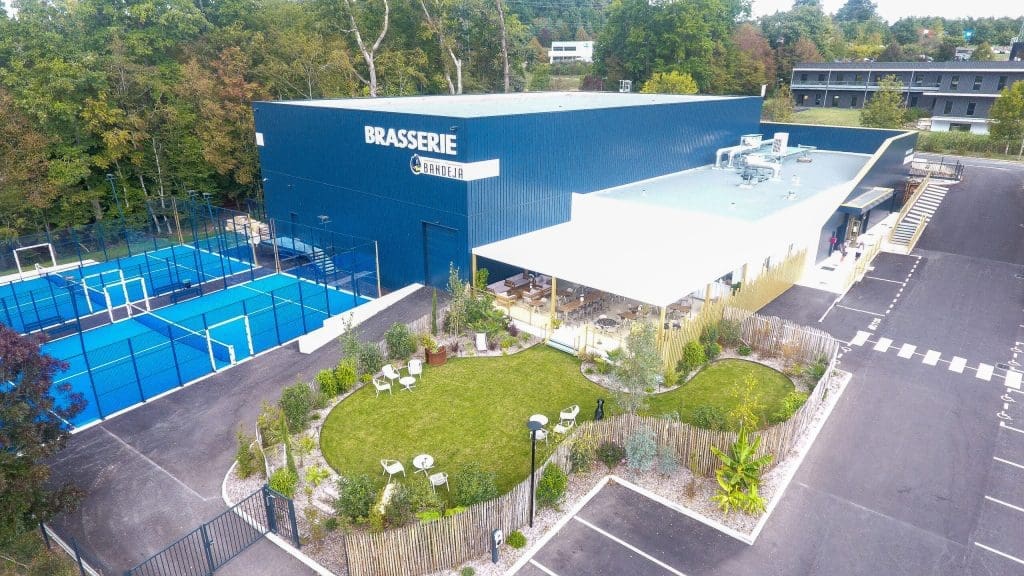 Aerial view of La Bandeja Brasserie and Padel Courts in Dordogne, featuring two blue outdoor courts and a spacious terrace with greenery.